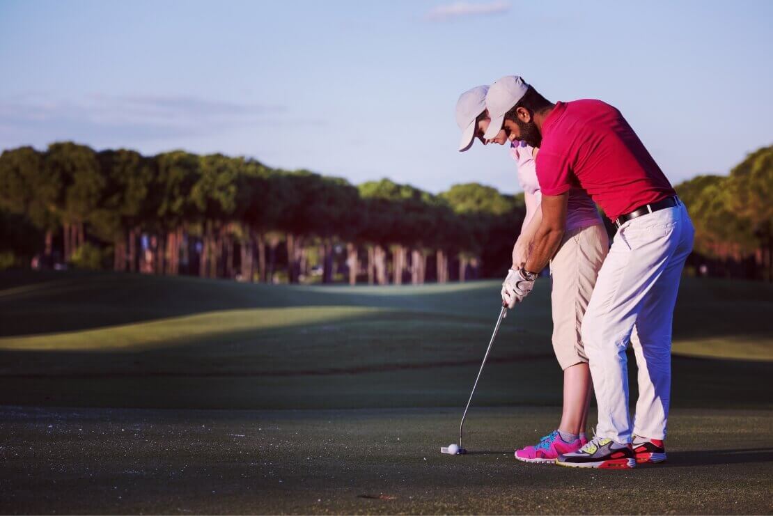 Golfspieler hilft Golfspielerin beim Schlag