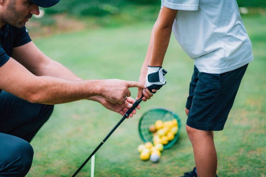 Golflehrer hilft einem Kind beim Abschlag