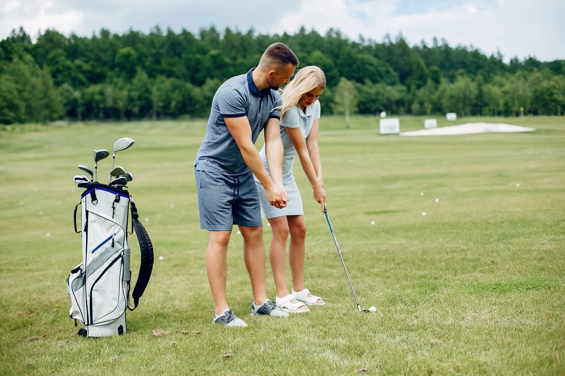 Ein Golfer zeigt seiner Golfpartnerin den richtigen Stand.