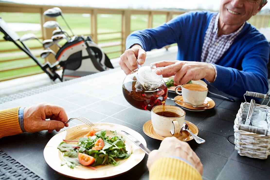 Golfer gießt seinem gegenübersitzendem Golfpartner bei einem gemeinsamen Essen eine Tasse Tee ein.