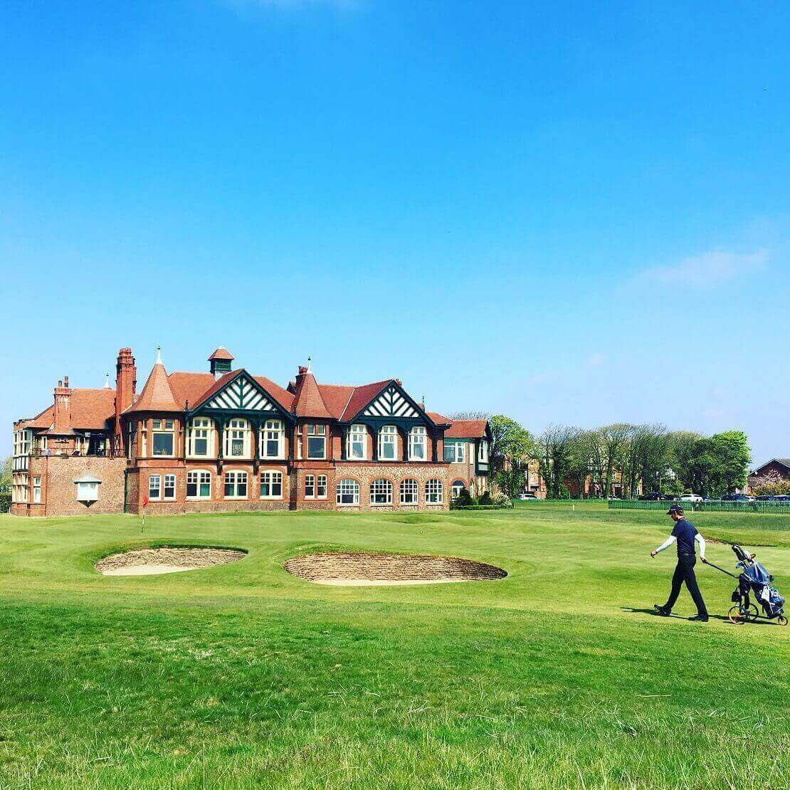 Backstein-Clubhaus des Royal Lytham & St. Annes Golf Club und ein Golfer mit Golftasche.