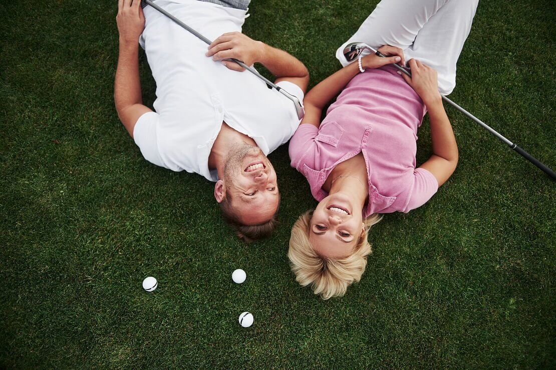 Pärchen liegt auf einem Golfplatz mit Golfbällen über dem Kopf