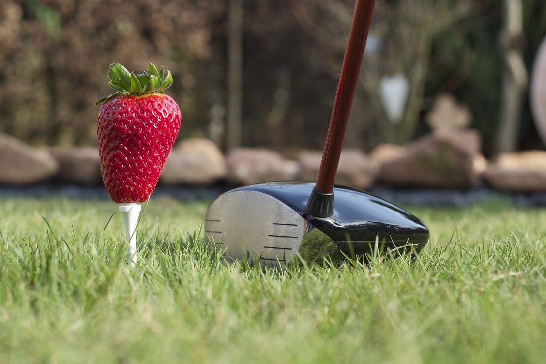 Erdbeere auf einem Tee neben einem Golfschläger