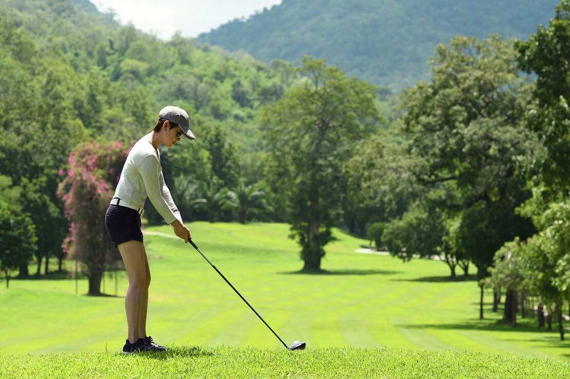 Eine Frau vor dem Abschlag des Golfballes auf dem Green eines Golfplatzes