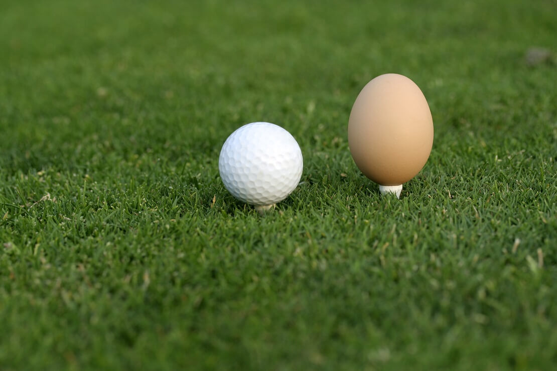 Golfball auf einem Golfplatz neben einem Ei