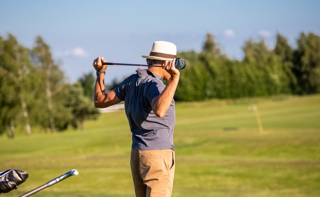 Mann hält einen Golfschläger hinter dem Rücken