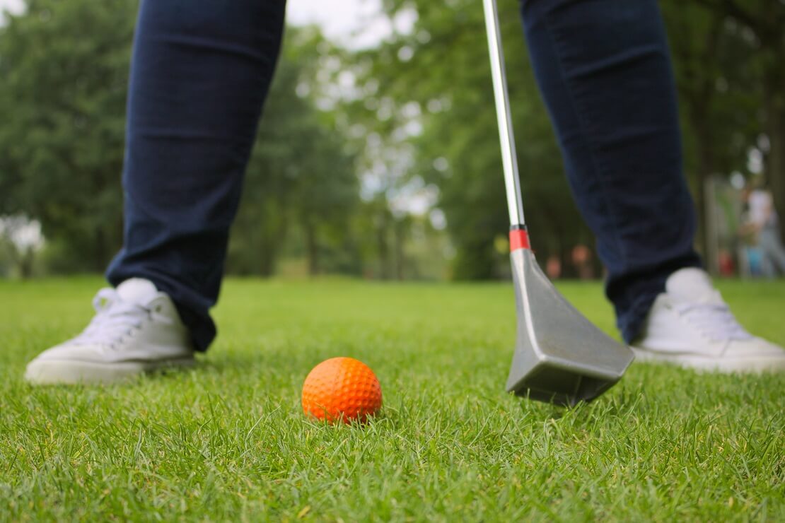 Golfer steht breitbeinig auf einer Grünfläche mit einem Swin-Golfschläger und einem Swin-Golfball zwischen seinen Beinen.
