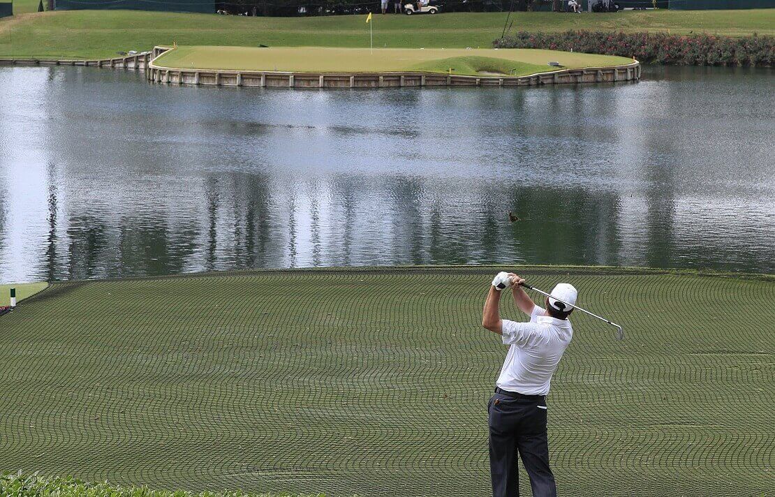 Golfspieler schlägt einen Ball am 17. Loch des Sawgrass Golf Club ab und schaut ihm über das Wasser hinterher.