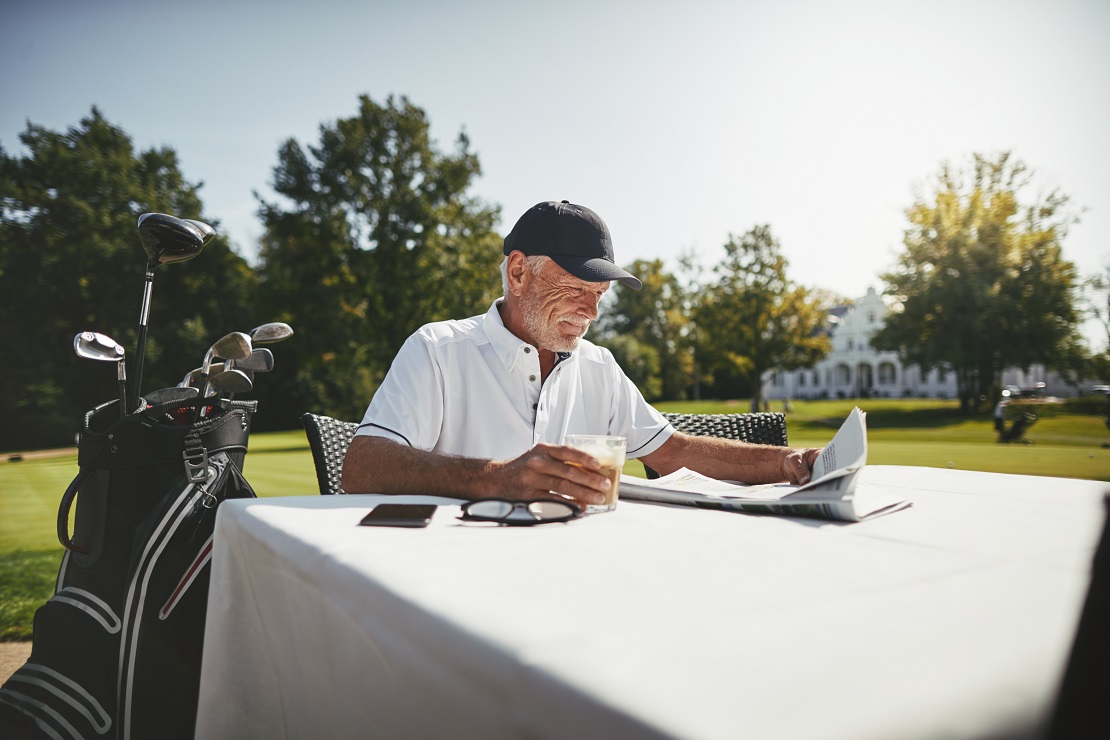 Ein Golfer sitzt an einem Tisch und Trinkt einen Kaffee dabei liest er eine Zeitung
