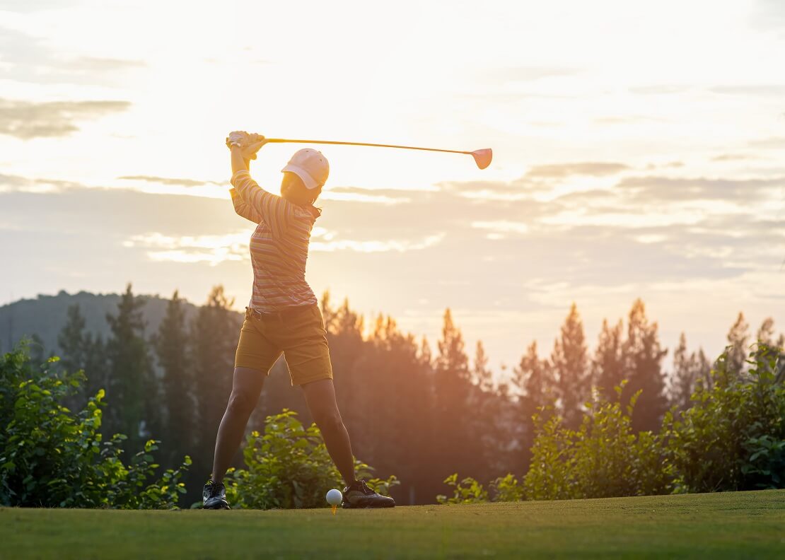 Golferin hält ihren Schläger vor dem Sonnenuntergang im Aufschwung über dem Körper