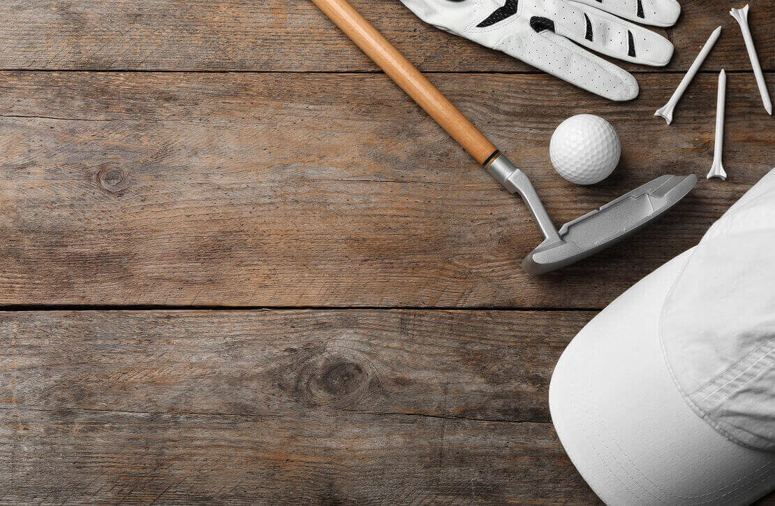 Auf Holzboden sind eine Mütze, ein Golfschläger, ein Ball, ein Handschuh und Tees ausgelegt.