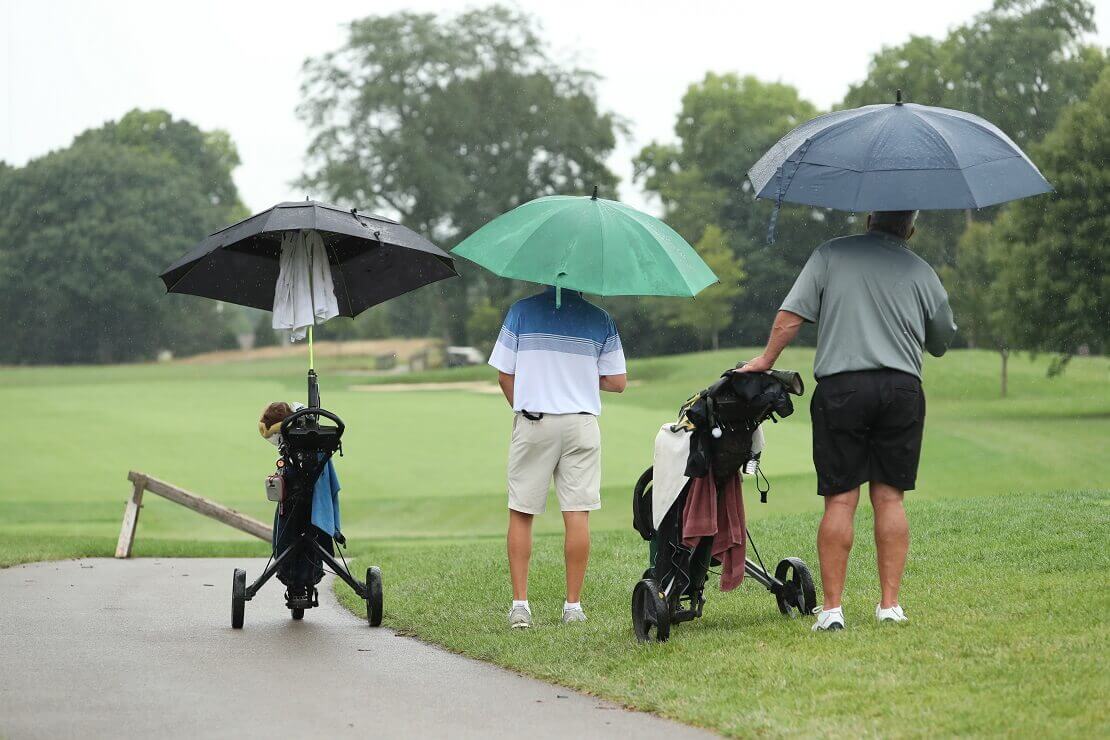 Golfer mit Schirm und Schirm über ihrem Trolley