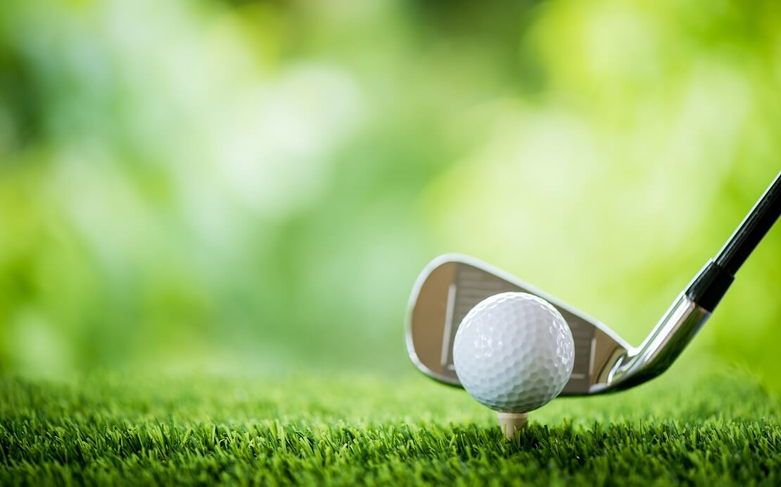 Golfball vor Golfschläger auf dem Grün mit grünem Farbspiel im Hintergrund