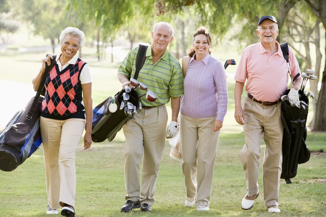 Eine Gruppe von vier Senioren-Golfern läuft freudestrahlend über den Golfplatz