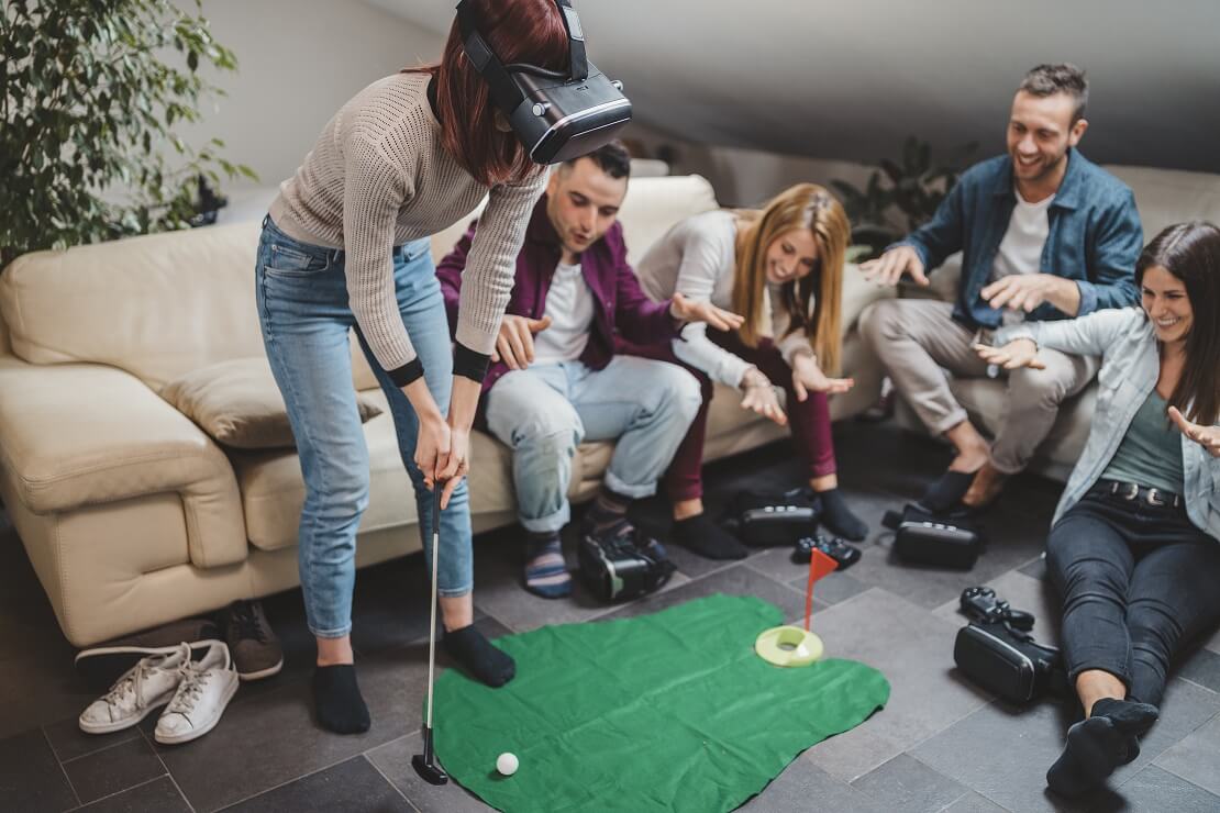 Frau steht mit einer VR-Brille in der Mitte einer Gruppe und spielt VR-Golf