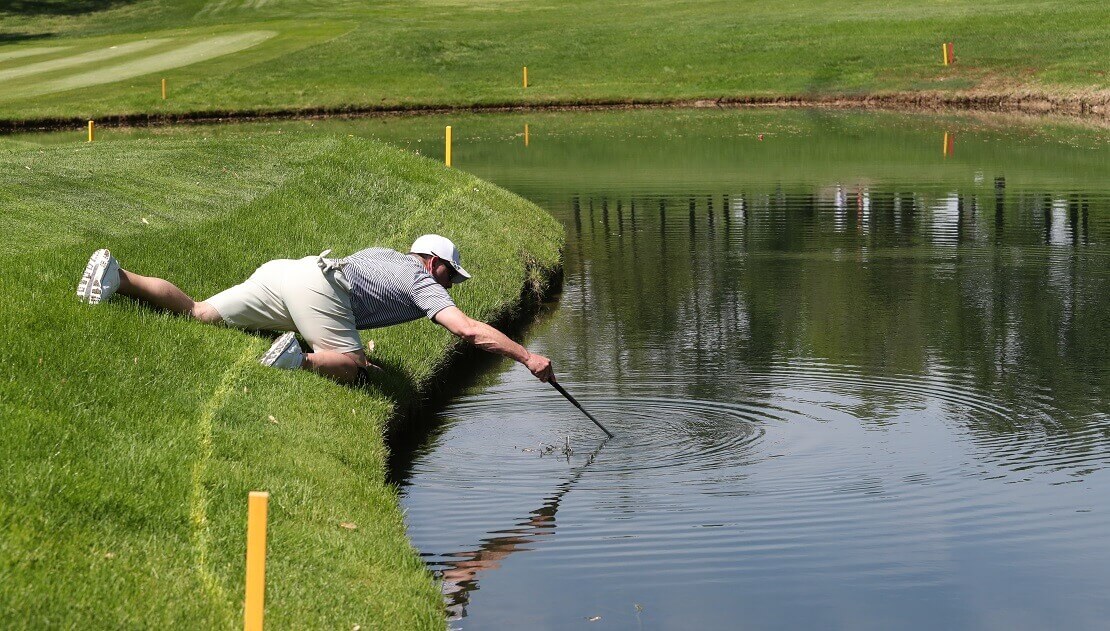 Golfer holt mit seinem Schläger den Ball aus einem Wasserhindernis