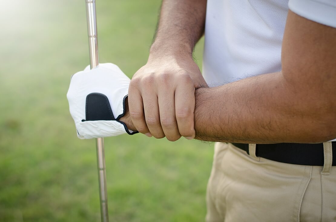 Golfer packt an sein Handgelenk in der anderen Hand trägt er einen Golfhandschuh und hält einen Golfschläger