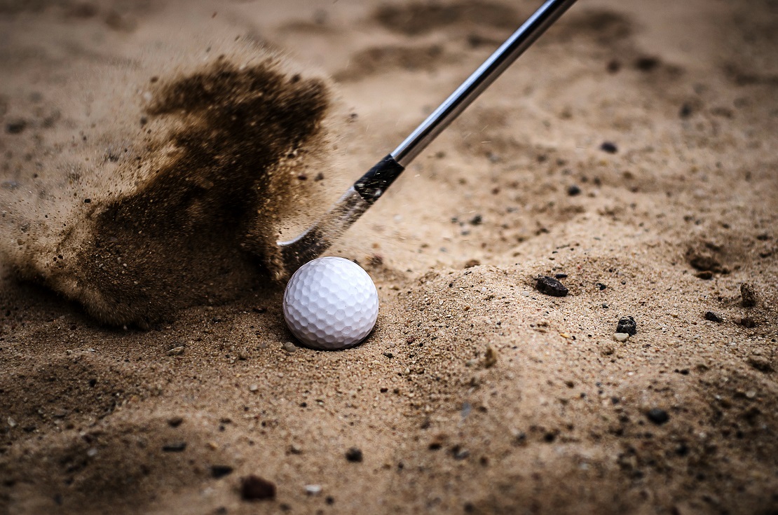 Golfball liegt im Sandbunker und wird von einem Schläger getroffen