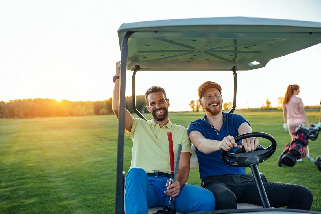 Zwei Golfer sitzen im Golfcart und lachen