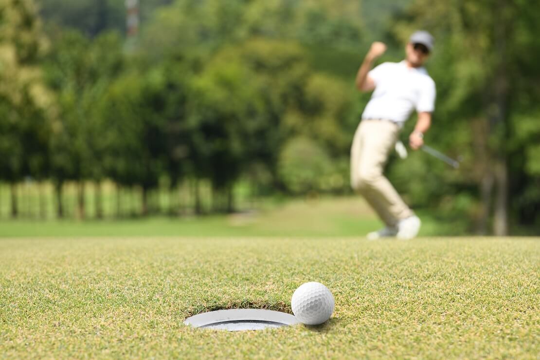 Golfball rollt ins Loch im Hintergrund jubelt der Golfer