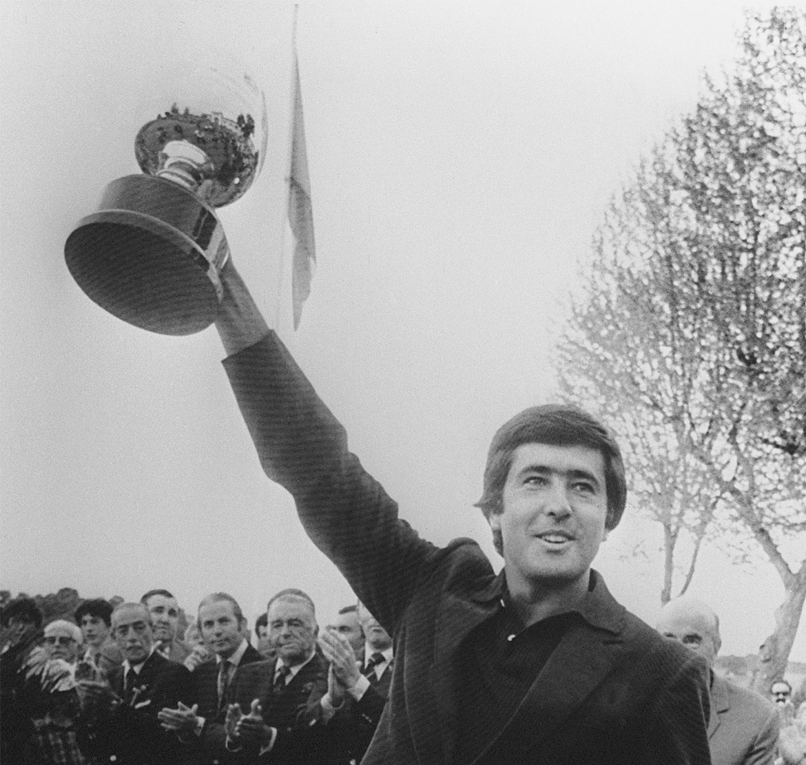 Severiano Ballesteros hält einen Pokal in der Hand hinter ihm stehen Menschen