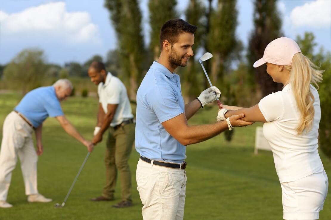 Golflehrer zeigt Schülerin die richtige Position der Arme