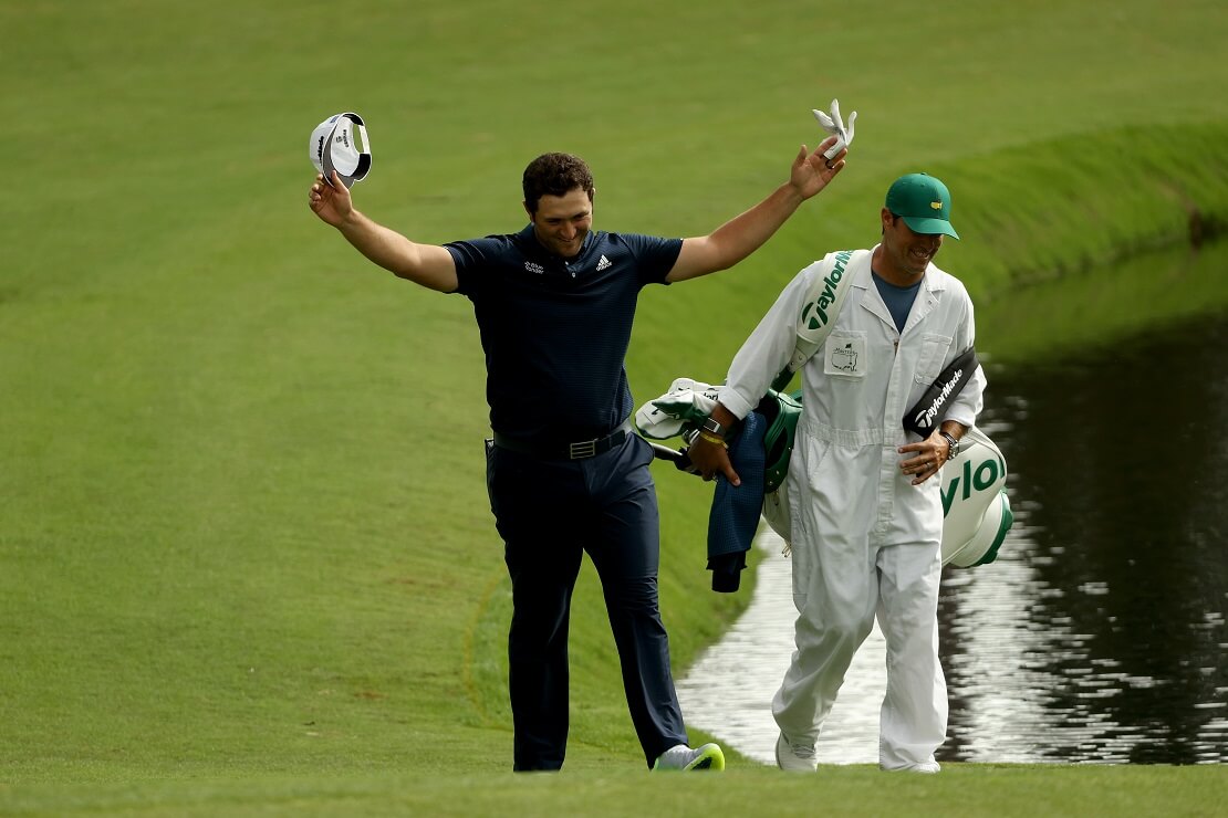 Jon Rahm hat die Kappe gezückt und verbeugt sich, dahinter der Caddie