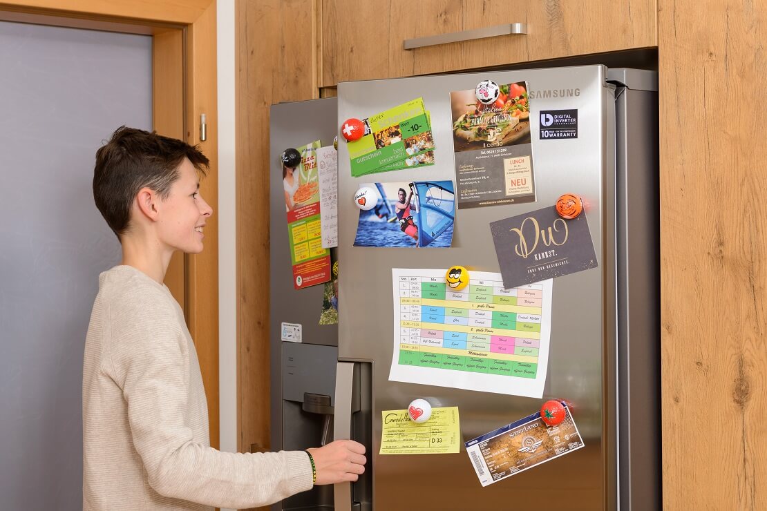 Junge öffnet den Kühlschrank, an dessen Tür magballs befestigt sind