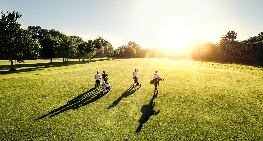 Sonne scheint auf einen Platz und vier Golfer laufen über ihn