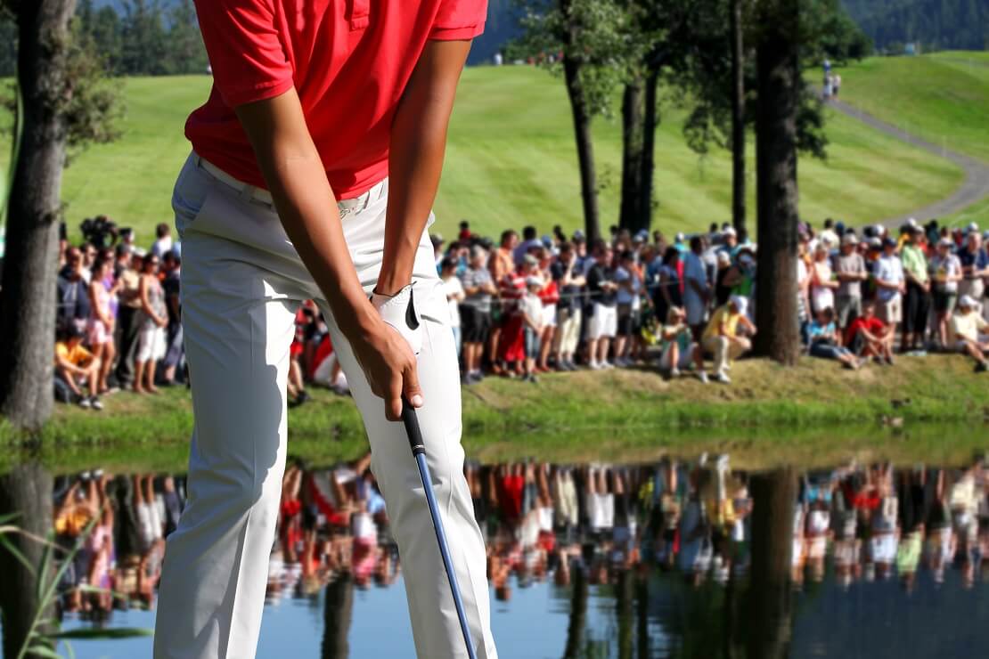 Hände und Beine eines Golfers vor dem Abschlag mit Publikum im Hintergrund