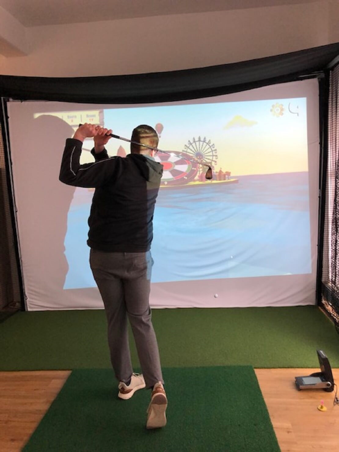 Golfer vor einem Golfsimulator spielt den Ball auf eine Dartscheibe