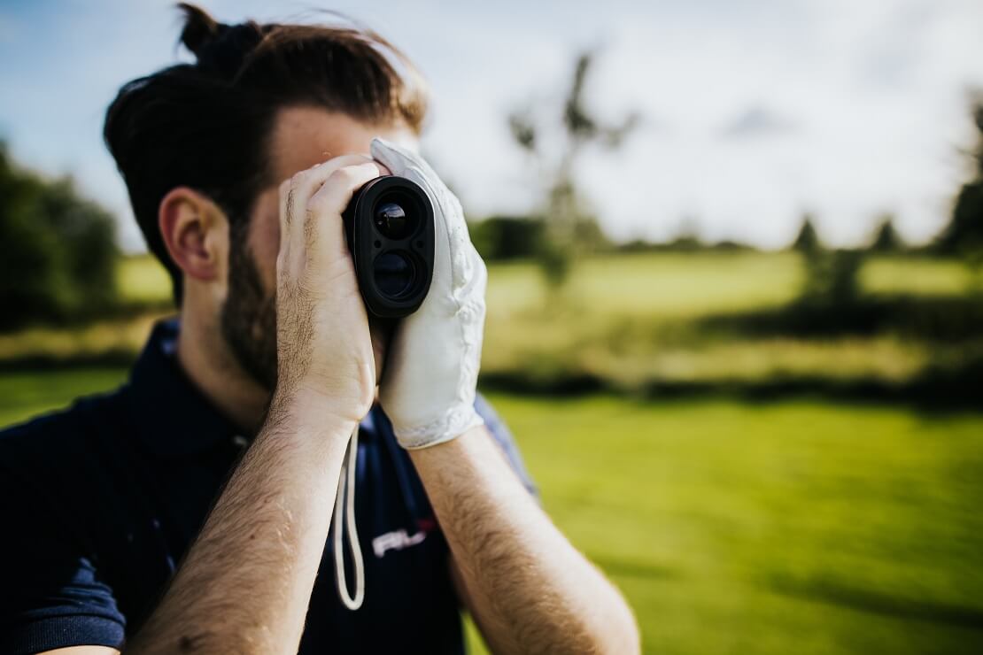 Golfer schaut durch einen Entfernungsmesser auf dem Golfplatz