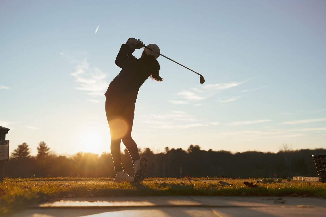 Eine Spielerin schlaegt auf der Driving Range vor dem Sonnenuntergang ab