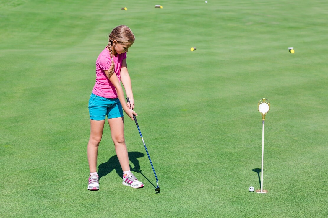 Ein Mädchen spielt den Golfball ins das Loch