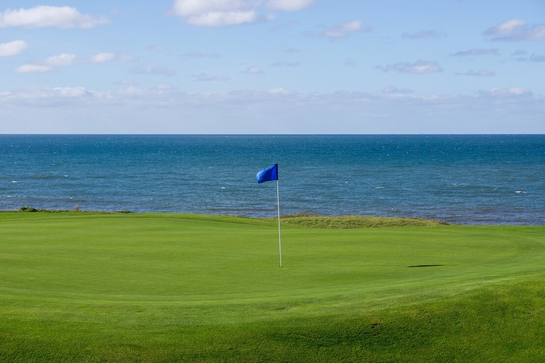 Golfplatz am Meer mit einer blauen Flagge auf dem Grün