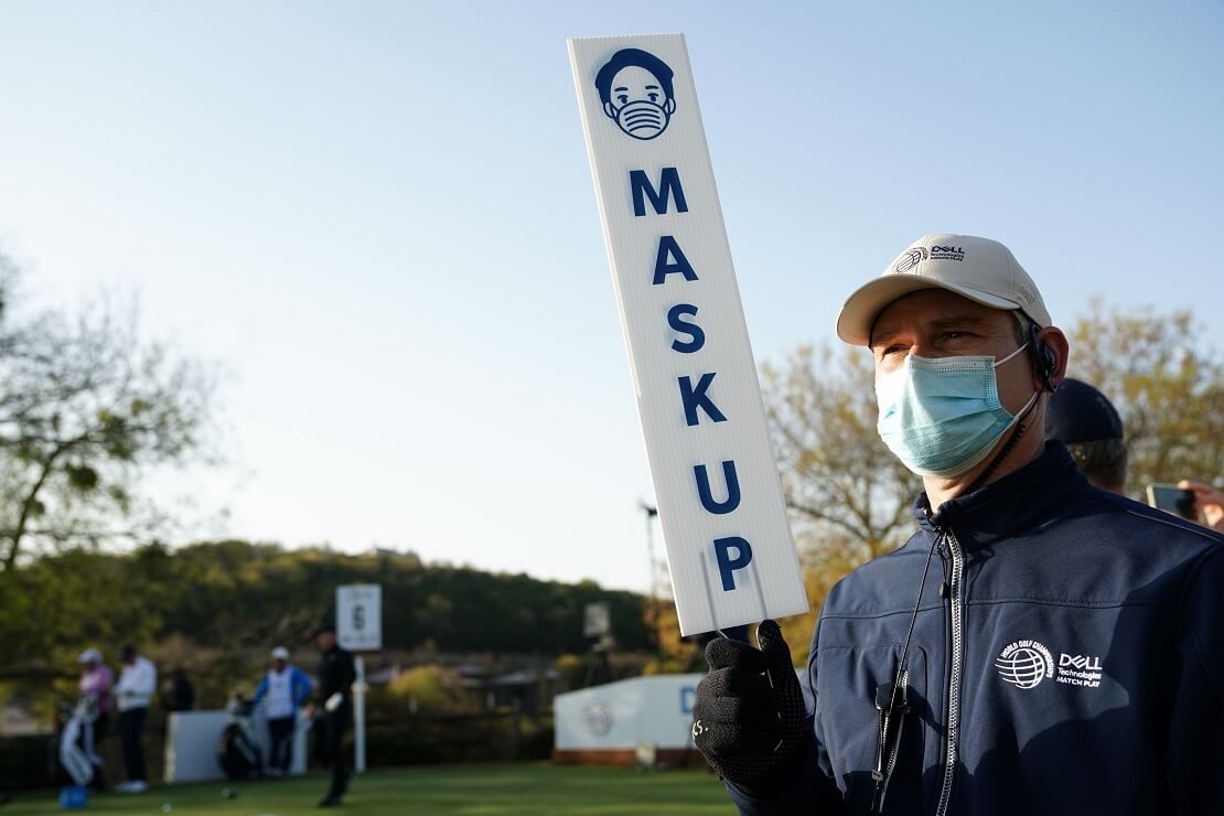 Turnier-Mitarbeiter mit Maske trägt ein Schild mit "Maske auf"