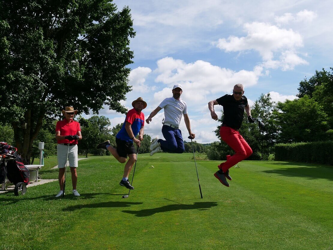 Drei Golfer springen in die Luft, ein vierter guckt zu