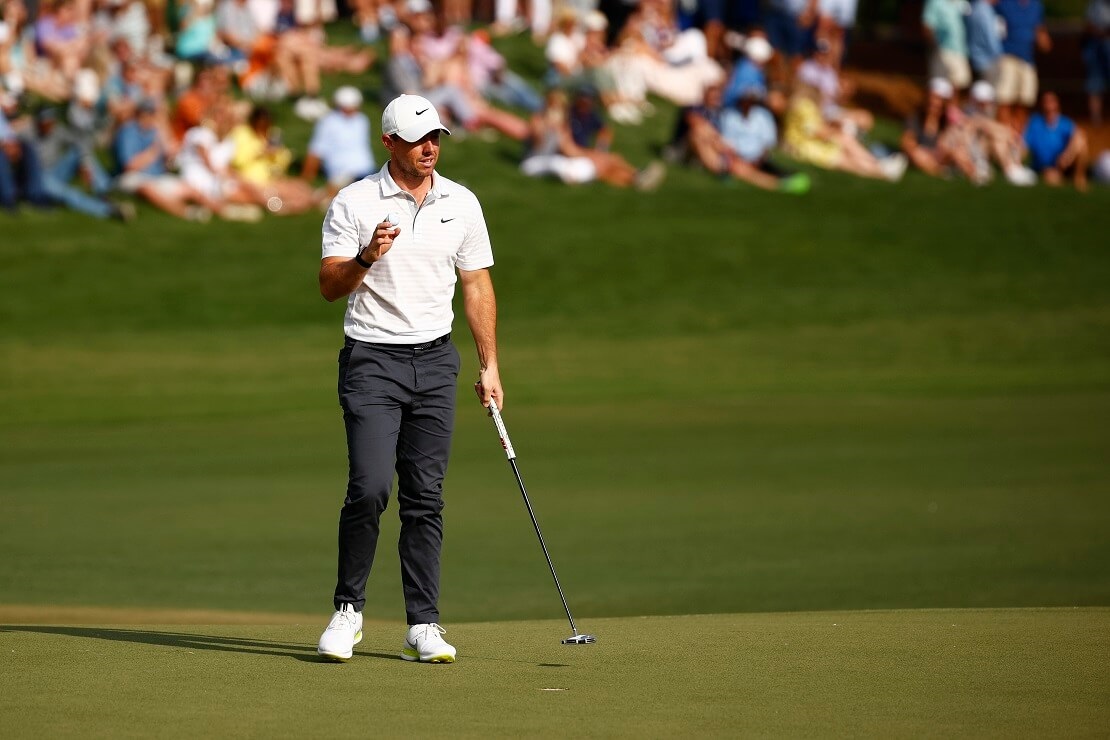 Rory McIlroy steht mit Ball und Schläger auf dem Grün vor Fans