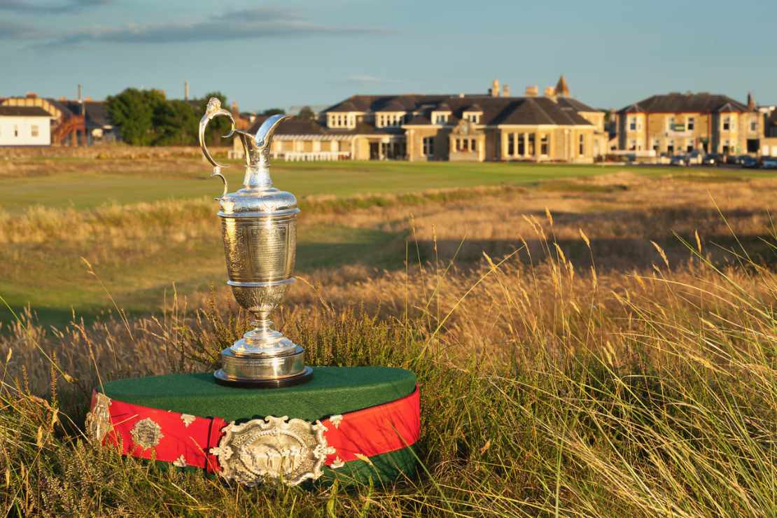 Ein Pokal steht auf einem Golfplatz, im Hintergrund das Clubhaus