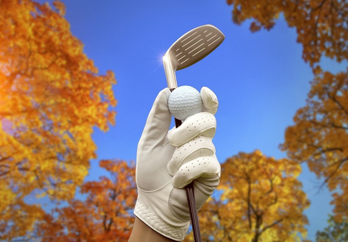 Golfschläger wird in die Luft gereckt mit herbstlichen Bäumen und blauem Himmel im Hintergrund