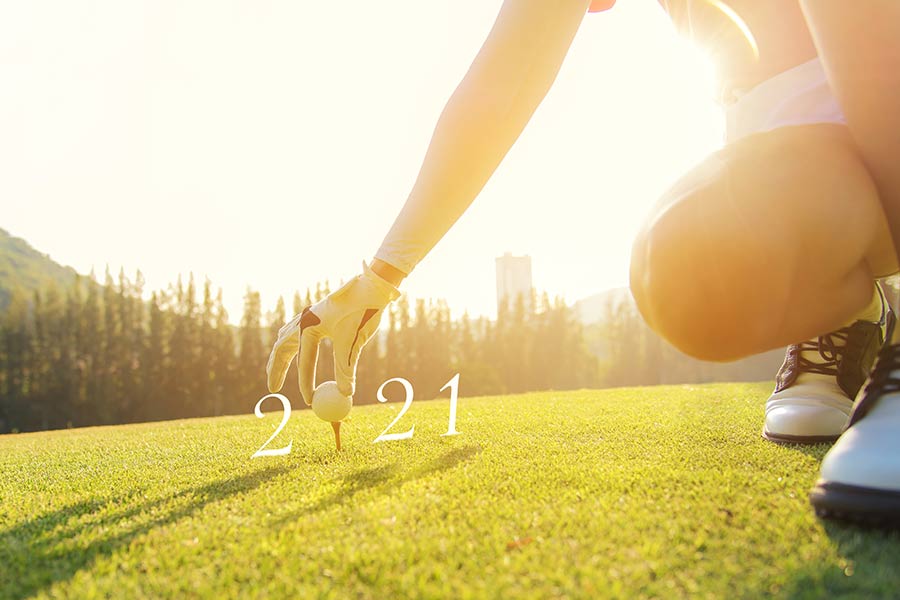 Golferin platziert einen Golfball auf dem Tee, der die 0 des Schriftzugs "2021" bildet