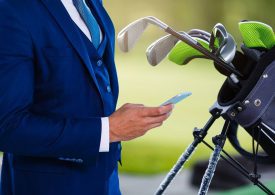 Geschäftsmann im Anzug mit Handy in der Hand und Golf-Equipment