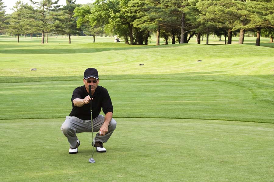 Golfer auf dem Grün hält seinen Putter vor sich