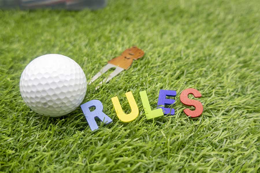 Golfball "Rules" und Pin auf Rasen