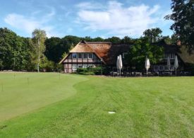 Ein Golfplatz im Hintergrund ein Haus mit Sitzmöglichkeiten zum Essen