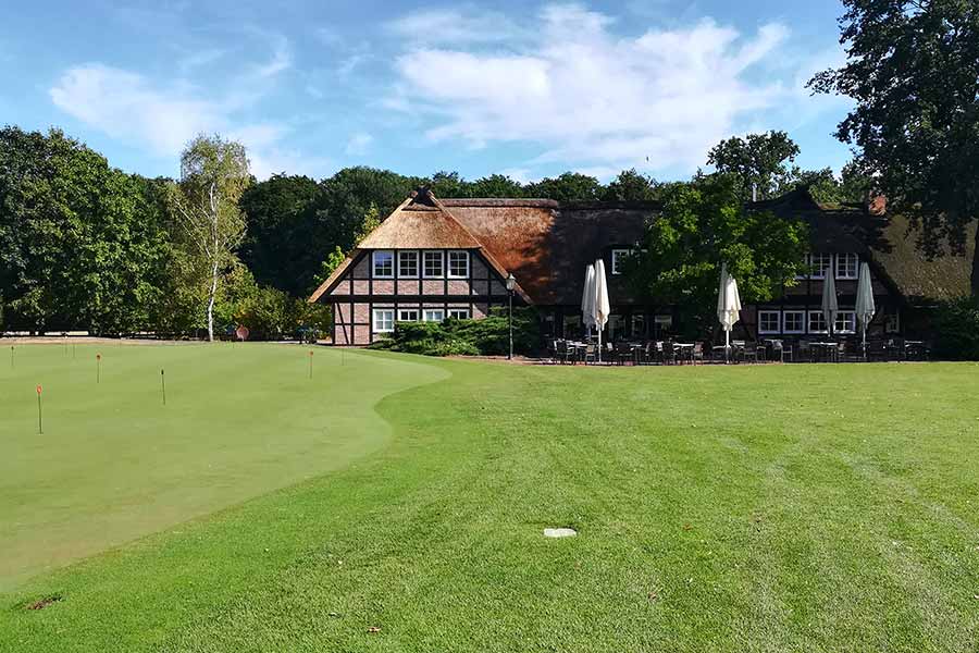 Ein Golfplatz im Hintergrund ein Haus mit Sitzmöglichkeiten zum Essen