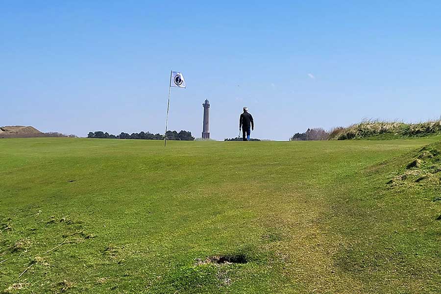 Grüner Golfplatz, im Hintergrund ein Mann und eine Golffahne