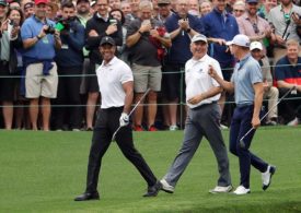 Tiger Woods, Fred Couples und Justin Thomas laufen mit Golfschlägern in der Hand zusammen zum nächsten Tee, im Hintergrund Fans