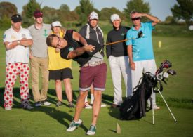 Sieben Golfer stehen in einem Halbkreis, einer Schlägt den Ball.