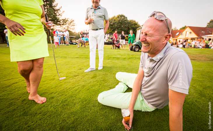 Ein Golfer sitzt mit einem Glas Bier auf dem Boden und lacht